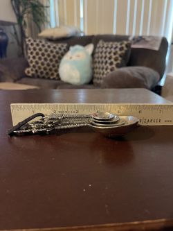 This item is a set of vintage-style ornate pewter measuring spoons featuring a whimsical tea theme. Each spoon is uniquely embossed with detailed desi