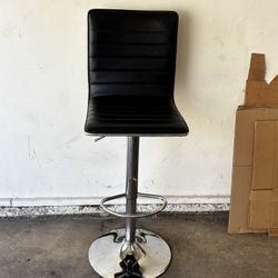 Black faux leather bar stool with a chrome-plated adjustable base and footrest.