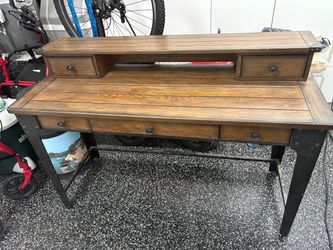 Industrial-style writing desk with a plank-top wood surface, black metal legs, and three lower drawers with ring pulls. Includes a raised hutch sectio