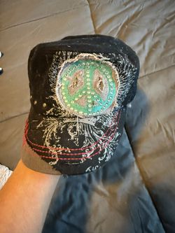 black distressed cadet-style cap featuring a rhinestone-embellished peace sign and embroidered wing details