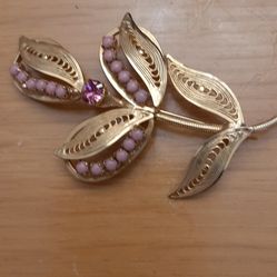 flower brooch  done in a gold finish in a cannetille filigree design and  set with mauve beads and a single mauve rhinestone