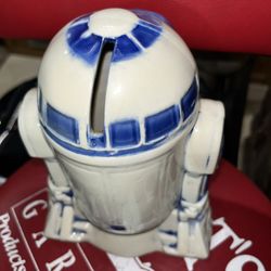 The image shows the bottom of a vintage R2-D2 ceramic coin bank.  The text molded into the ceramic indicates it is a piece of official merchandise fro