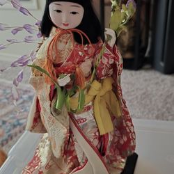 The doll in the image is a traditional Japanese doll, dressed in a very ornate  hand-made kimono.