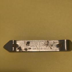 Vintage LUCKY LARGER BOTTLE OPENER. Bottom side Reads - It’s Lucky when you live in America/ Top side Reads- LUCKY LARGER- AGED DATED BEER. 
