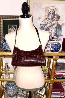 Baguette-style bag with a glossy crocodile-effect finish in a wine-colored tone. It features a minimalist, curved design popular in fashion-inspired