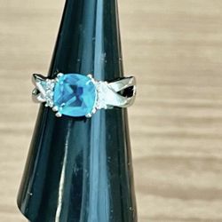Elegant blue cushion-cut center stone set in a polished silver band. Stamped 925 Sparkling accent stones flank the center for added brilliance. Classi