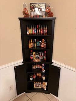 Black Corner Cabinet with Storage Shelves with hot sauces as shown