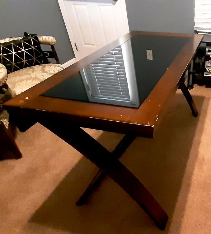 rectangular wooden table with a black glass inlay top and X-shaped legs.