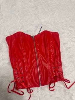 Bold red faux leather corset top with front zip closure. Lace-up sides add adjustable shaping and a flattering silhouette. Smooth finish for a sleek,