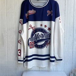 camiseta tipo jersey estilo deportivo blanca con detalles en azul y rojo que presenta el texto "CALIFORNIA" y el número "23", similar a los modelos co