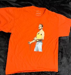 This vibrant orange graphic T-shirt features an iconic image of Freddie Mercury, the legendary frontman of the rock band Queen.