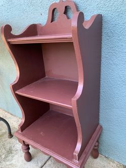 A painted wooden three-tiered shelf unit with decorative top and turned legs.