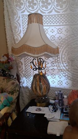 vintage-style table lamp features a distinctive amber glass body and a ornate, fringed fabric shade.