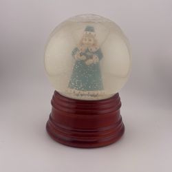 The Maud Humphrey Snow Globe "Winter Days" is a figurine featuring a traditional style, depicting snow in a winter scene. This collectible decorative 