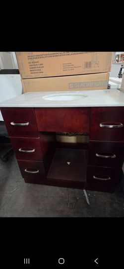 Dark wood-finish bathroom vanity has a white marble-style countertop with an integrated oval sink. This unit is an American Standard brand and feature