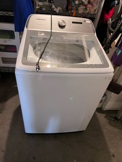 This white Samsung washing machine appears to be a 4.9 or 5.0 cu. ft. top-load model. ® • It features an agitator or impeller system designed to reduc
