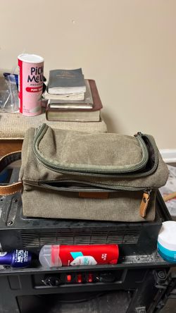 This khaki green canvas toiletry bag features dual zippers and a small leather brand patch.
