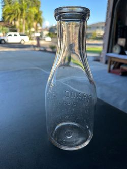Vintage, clear glass one-quart milk bottle features embossed lettering that reads "ONE QUART LIQUID”