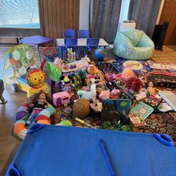 Four mattresses, a table with four chairs, a chair with a table, a colored chair, teddy bears, toys, boxes, a ball, toy animals, and a musical mat.
