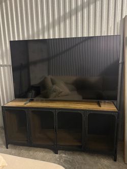 consola de TV de estilo industrial (estructura de metal negro con 4 puertas de malla metálica y cubierta en tono madera clara/rústico)