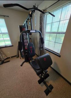 FITNESS Multi-station home gym with lat pulldown bar, adjustable weight stack, padded seat and back rest, leg developer, and low pulley cable system. 