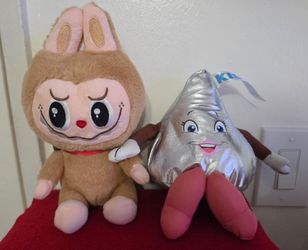 The left plush is a Labubu figure from the The Monsters series by Pop Mart, The right plush is a Hershey's Kiss character, which may be part of a bran