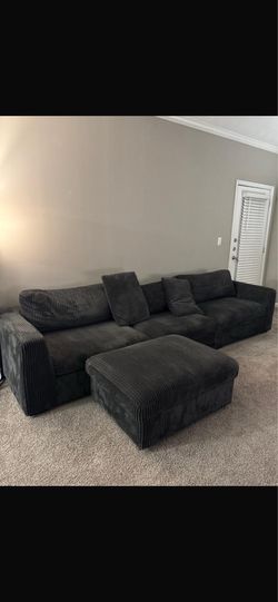 Modern oversized dark grey corduroy sectional couch with matching ottoman.