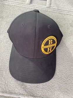 black baseball cap with a round yellow and black "Bragg Crane & Rigging" patch