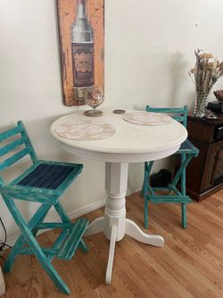 White high-top bistro table w/2 Turquoise high wWooden chairs.