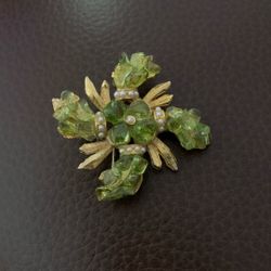 This vintage brooch features green molded rhinestones, faux pearls, and gold-tone metal, likely from the 1960s. 
