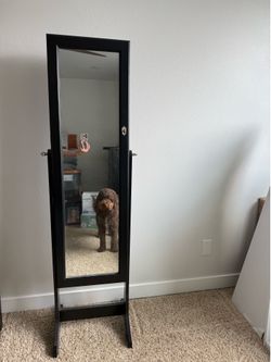 Black freestanding cheval jewelry armoire with a full-length tilting mirror.