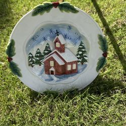 This is a vintage 3D ceramic plate with a Christmas church and winter scene. The plate is decorated with holly berries and leaves around the rim.