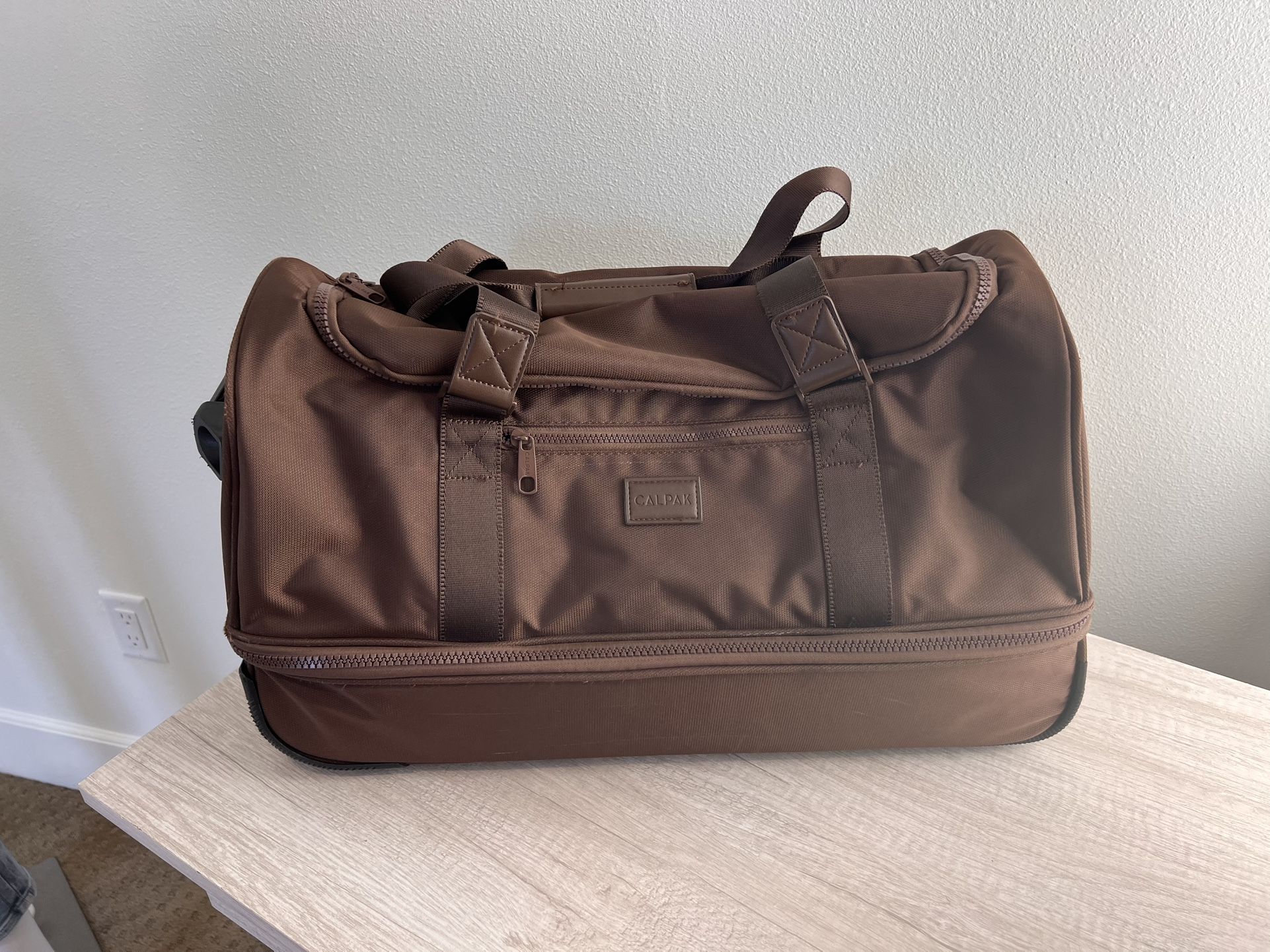 Calpak Stevyn Brown rolling duffel, a versatile blend of duffel bag functionality and wheeled luggage 22” 