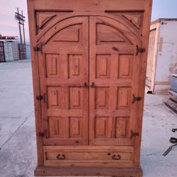 Mexican pine armoire, nandcrafted from solid pine wood and featuring traditional cathedral-style doors and dark iron hardware.