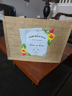 Stylish beige canvas tote with vibrant yellow and pink rose accents. Durable construction and roomy interior for everyday use. Bright floral detail ad