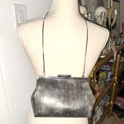 This bag is a Calvin Klein evening clutch with a brushed metallic finish in gunmetal gray. It features a structured design with a snap closure at the 