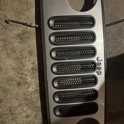 used, genuine OEM Mopar front grille in Bright Silver Metallic (paint code PSB/PSC) for a Jeep Wrangler JK or JKU model year 2007-2018.
