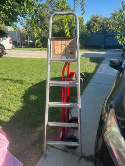 Durable aluminum step ladder has four steps and a top platform with a safety rail. This lightweight ladder is paired with a heavy-duty red metal hand