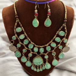 It features two cascading tiers of oval and teardrop turquoise stones. It is accented with small dark brown wooden spacer beads along the col
