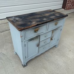 distressed, light blue and black painted wooden accent cabinet features a dark antiqued wood top, multi-drawer configuration, and lower cabinet doors.