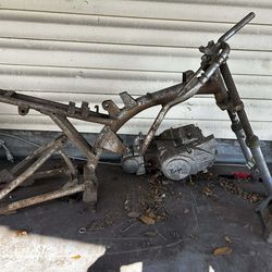 Rusty Baja dirt bike frame with an engine and front forks. Engine has 'Baja' written on it. Good for a project or for parts.y