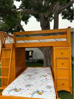 The wooden bunk bed includes both mattresses and features an office desk, five drawers, and a bookshelf.