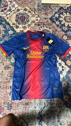 This Nike FC Barcelona 2012-2013 home jersey features the iconic blue and red gradient design and the "Qatar Foundation" sponsor logo.