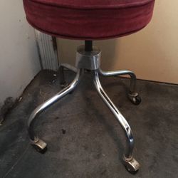 A ROUND STOOL ON WHEELS 22” INCHES TALL 15” INCHES WIDE 3” INCHES THICK CUSHION $35.00