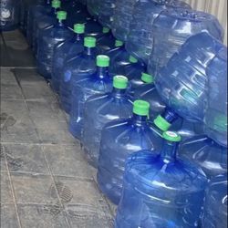 4 Gallon blue water jugs with green caps.