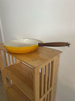 A vintage Copco Denmark yellow enameled cast iron skillet with a wooden handle, designed by Michael Lax