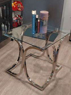 modern accent table featuring a clear square glass top and a sleek, polished chrome base with a unique curved leg design, making it a stylish piece th