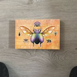 a makeup palette featuring an Egyptian scarab beetle design. K