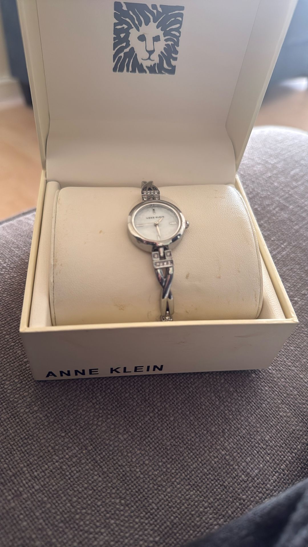 Anne Klein silver-tone women's watch with a mother-of-pearl dial and a twisted bangle bracelet accented with premium crystals.