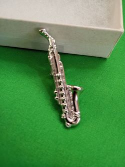 Polished silver-toned metal tie clip in the shape of a saxophone.